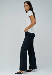 Camiseta blanca de manga corta combinada con jeans de pierna ancha azul oscuro y tacones negros de punta, sobre un fondo claro y liso.