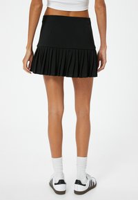 Zwarte plissé rok met een aansluitende taille en gelaagd ontwerp. Gemaakt van textuurstof, gecombineerd met witte sportieve schoenen en sokken.