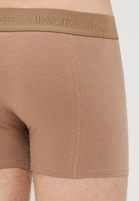 Braune, enganliegende Boxershorts mit sichtbaren Nähten und einem elastischen, gebrandeten Bund, getragen von einer Person.