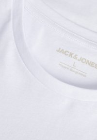 T-shirt bianco in cotone con scollatura rotonda, caratterizzato da una consistenza morbida e un'etichetta del marchio "JACK & JONES" stampata in oro chiaro all'interno.
