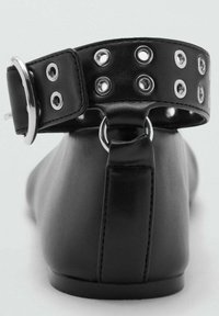 Ballerine in pelle nera con una larga fascia alla caviglia, caratterizzate da occhielli in argento e un dettaglio ad anello in metallo, texture liscia e forma curva.