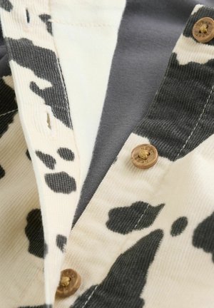 Țesătură alb-negru cu model de vacă și textură nervurată, având nasturi maro la guler și un strat interior solid gri.
