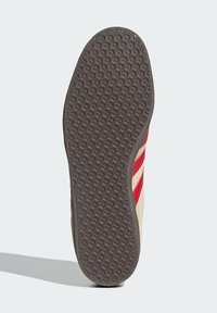 Σόλα παπουτσιού με υφασμένη καφέ καουτσούκ βάση που διαθέτει σχέδιο με κηρήθρα· επάνω μέρος σε μπεζ απόχρωση με κόκκινες ρίγες κατά μήκος των πλαισίων.