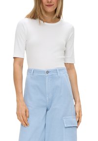 Weißes kurzärmliges, eng geschnittenes T-Shirt, kombiniert mit hellblauen, hoch sitzenden Cargo-Hosen mit seitlichen Taschen und Knopfverschluss.