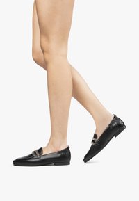 Mocassini in pelle nera dal design elegante, con una cinghia decorativa e dettagli di cucitura discreti; tacco basso e retro elasticizzato per maggiore comfort.