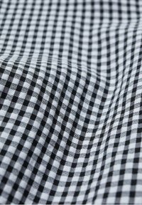 Czarnobiała tkanina w kratkę gingham z wzorem w kratkę. Tekstura wydaje się tkana, z gładkim wykończeniem, ukazując wyraźne kwadraty.