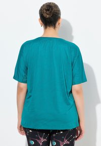 Top de manga corta en verde azulado con una textura suave, que presenta patrones sutiles. Combinado con leggins negros que exhiben diseños cósmicos coloridos.