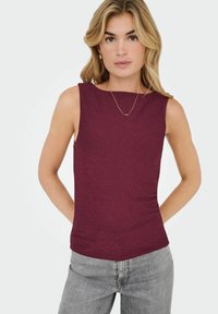 Bordeaux ærmeløs top med bådudskæring, tekstureret stof og en tætsiddende form. Sættes sammen med grå jeans og en minimal guld halskæde som accent.