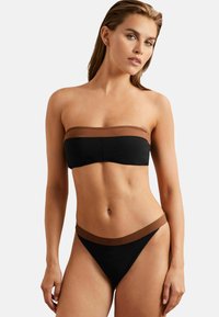 Crni bikini s smeškastim akcentima. Top bez naramenica ima glatki pojas. Donji deo ima sličan pojas u struku. Materijal izgleda lagano i rastezljivo.