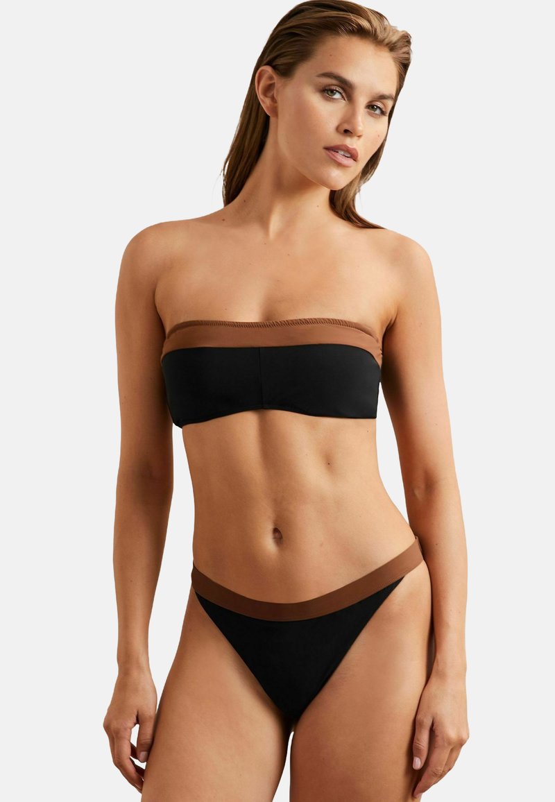 Crni bikini s smeškastim akcentima. Top bez naramenica ima glatki pojas. Donji deo ima sličan pojas u struku. Materijal izgleda lagano i rastezljivo.