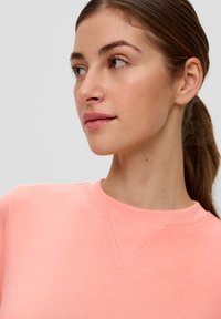 Licht koraalkleurig sweatshirt met een geribbelde ronde hals en driehoekige stikseldetails. Gladde textuur en een relaxte pasvorm, met een zacht stoffen uiterlijk.