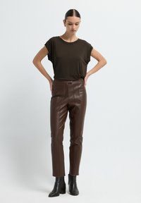 Bruine nep leren broek met een gestroomlijnd ontwerp en verticale naden, gecombineerd met een losvallend donkerbruine top. Zwarte hoge enkellaarsjes.