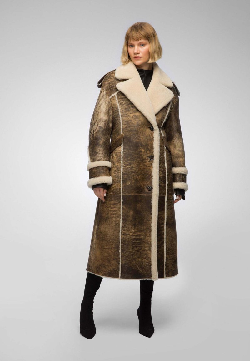 Brown shearling coat with a cream collar and cuffs, featuring a long, straight design, button closure, and contrasting white stitching.