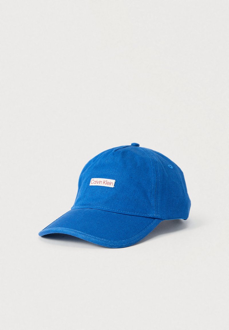 Casquette de baseball en coton bleu avec une visière courbée et une étiquette rectangulaire blanche portant l'inscription "Calvin Klein" en rouge.