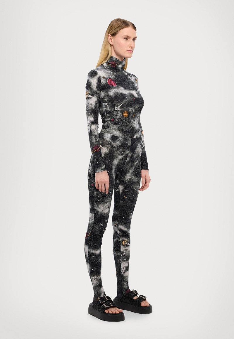 Bodysuit ajustado en negro y gris con un estampado de galaxia, que presenta planetas y estrellas coloridos, combinado con sandalias de plataforma negras y gruesas.