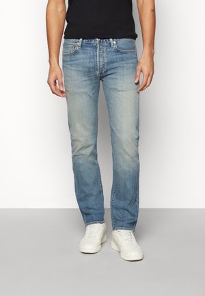 Helle blaue Denim-Jeans mit schmalem Schnitt, ausgestattet mit einem klassischen Fünf-Taschen-Design und dezentem Verblassen. Getragen mit weißen Turnschuhen.