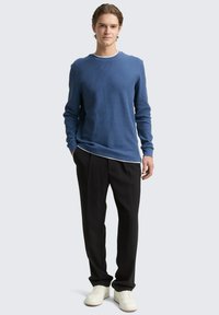 Blaues, langärmeliges, geripptes Sweatshirt kombiniert mit schwarzen Hosen und weißen Turnschuhen. Das Outfit hat eine lockere Passform und schichtete Designdetails.