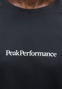 Κοντινό πλάνο μαύρου μπλουζακιού με λευκή επιγραφή "Peak Performance" στο κέντρο του στήθους.