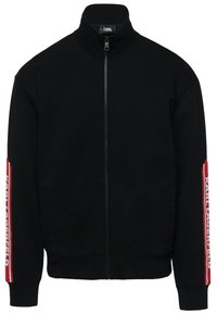 Chaqueta negra con cierre de cremallera y cuello alto, puños elásticos y bolsillos laterales. Presenta la marca "KARL LAGERFELD" en rojo y blanco en las mangas. Textura suave.
