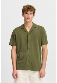 Camisa de botones de manga corta en verde oliva, confeccionada en una tela suave con un corte relajado, que presenta un cuello con muesca y un sutil detalle de logo.
