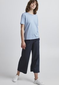 Lichtblauw katoenen t-shirt met een ronde hals, gecombineerd met marineblauwe wijde broek en witte sneakers. Eenvoudig, ontspannen pasvorm design.