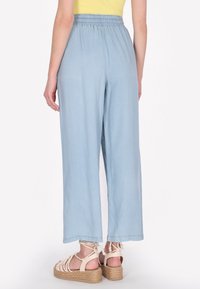 Lichtblauwe wijde broek met een elastische tailleband, gemaakt van een zacht materiaal. Gepaard met beige espadrille-sandalen.