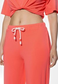 Korallrosa avslappnade byxor med dragsko i midjan, med en jämn textur och två sidofickor för bekvämlighet.