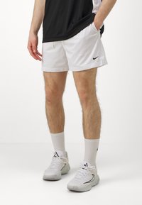 Baltos sportinės šortai su tinklinėmis tekstūromis, su juodu Nike logotipu. Suderinti su baltais kojiniais ir lengvais batais su juodais akcentais.