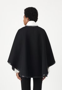 Juodas apsiaustas su lygiu paviršiumi, turintis baltą apykaklę ir juodą apdailą kraštuose. Elegantiškai gula ant pečių.