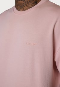 Light pink cotton T-shirt with a crew neck, featuring embossed logo "ESTEEM" on the front. Smooth texture and relaxed fit design.