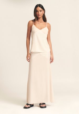 Lichtbeige satijnen cami-top met dunne bandjes, gecombineerd met een bijpassende maxi-rok. Gladde textuur, minimalistisch ontwerp, met een subtiele draai op de taille.