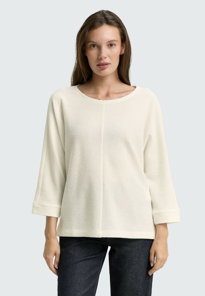 Lichtromige gebreide top met een textuurpatroon, ronde halslijn en driekwartmouwen. Gecombineerd met donkere denim jeans.