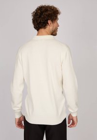 Pull en maille blanc avec de longues manches, des bords côtelés au niveau des poignets et de l'ourlet, et une coupe décontractée. Texture lisse ; design minimaliste sans motifs ni accents.