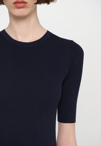 Top in maglina a coste blu navy con scollatura rotonda e maniche corte. Texture liscia con una silhouette aderente. Colore uniforme senza motivi o dettagli.