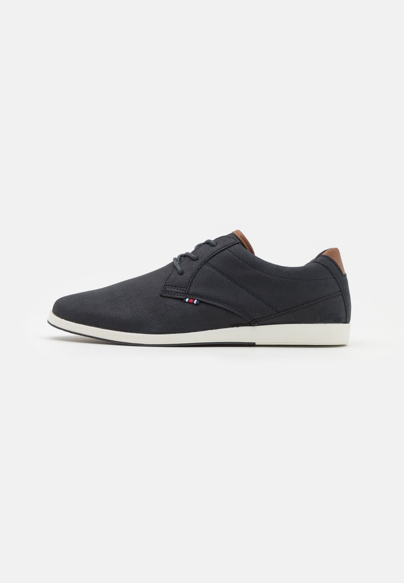 Chaussure décontractée noire pour homme à lacets, avec semelle blanche et accents marron sur le talon et la languette, présentée en profil latéral sur fond blanc.
