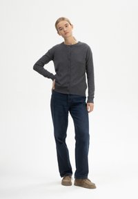 Grau cardigan mit rundem Ausschnitt, vorderem Knopfverschluss und gerippten Bündchen, kombiniert mit dunkelblauen Jeans und beigen Schuhen. Einfaches Design.