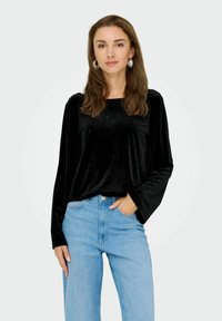 Top lungo in velluto nero con scollatura quadrata, abbinato a jeans azzurri a vita alta e orecchini a cerchio in argento.