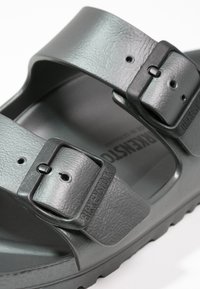 Sandales grises de style Birkenstock avec deux boucles réglables, des sangles texturées et une semelle intérieure moulée pour le confort. Semelle extérieure en caoutchouc visible.