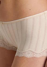 Pantaloni boyshorts beige in cotone con strisce verticali e un bordo in pizzo floreale sull'orlo. Texture liscia con un accento morbido in vita.