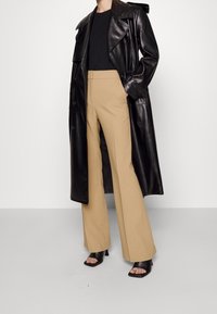 Svart läder trenchcoat, svart topp, beige vida byxor och svarta klackade mules. Slät textur, skräddarsydd passform och minimal hårdvara.