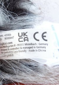 Textile label with mixed gray and black fur texture. Labels indicate product details and compliance with UKCA and CE standards.