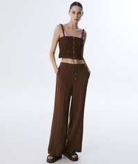 Top corto marrone arricciato con spalline rosa e chiusura a bottoni, abbinato a pantaloni marroni a vita alta e gamba larga e sandali chunky.