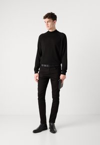 Pull noir à manches longues avec des manches raglan, associé à un jean noir ajusté, une ceinture noire et des bottines ; tenant une pochette noire.