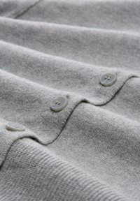 Helles graues gestricktes Sweatshirtgewebe mit horizontalen Rippstrukturen und drei runden hellgrauen Knöpfen entlang der Öffnung.