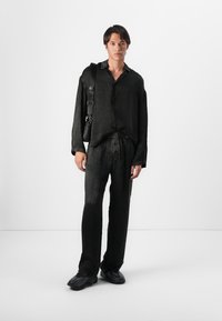 Chemise en lin noir et pantalon assorti, avec une coupe décontractée et une texture subtile. Porté avec un sac bandoulière noir et des chaussures foncées.
