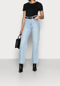 Ljust blå högmidjade jeans med rak ben, parat med en svart åtsittande t-shirt och ett svart bälte, håller en liten svart väska.