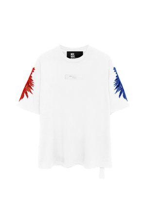 Camiseta blanca de manga corta con bordado rojo en la manga izquierda, bordado azul en la manga derecha y una pequeña etiqueta rectangular en el pecho.