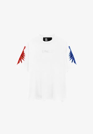 Camiseta blanca de manga corta con bordado rojo en la manga izquierda, bordado azul en la manga derecha y una pequeña etiqueta rectangular en el pecho.