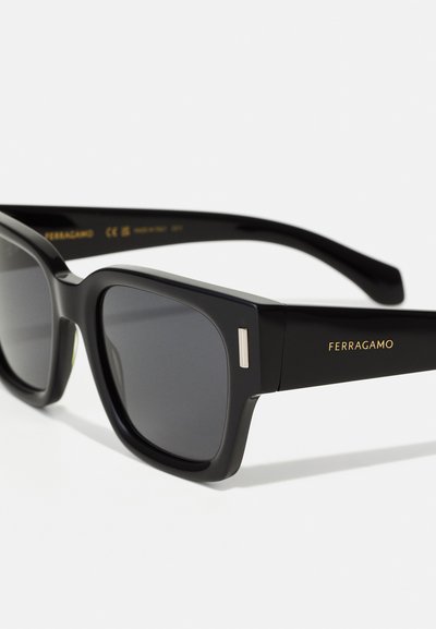 Occhiali da sole neri rettangolari con lenti scure, caratterizzati da montature in plastica liscia e un logo dorato Ferragamo sulla tempia.