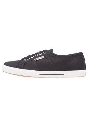 Baskets basses en toile noire avec semelle en caoutchouc blanche et lacets, avec un petit logo Superga sur le côté.